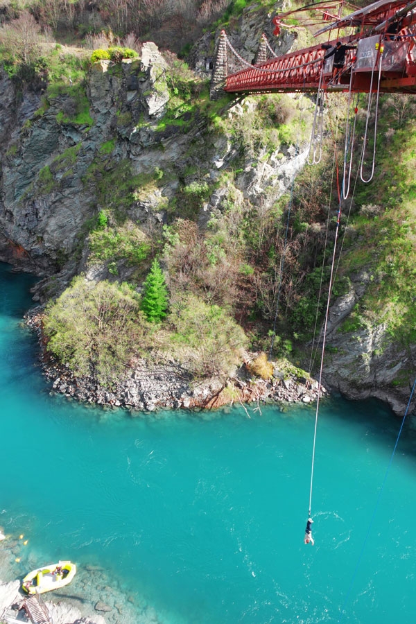 A person bungee jumping from a red bridge over a vivid river in Queenstown, New Zealand