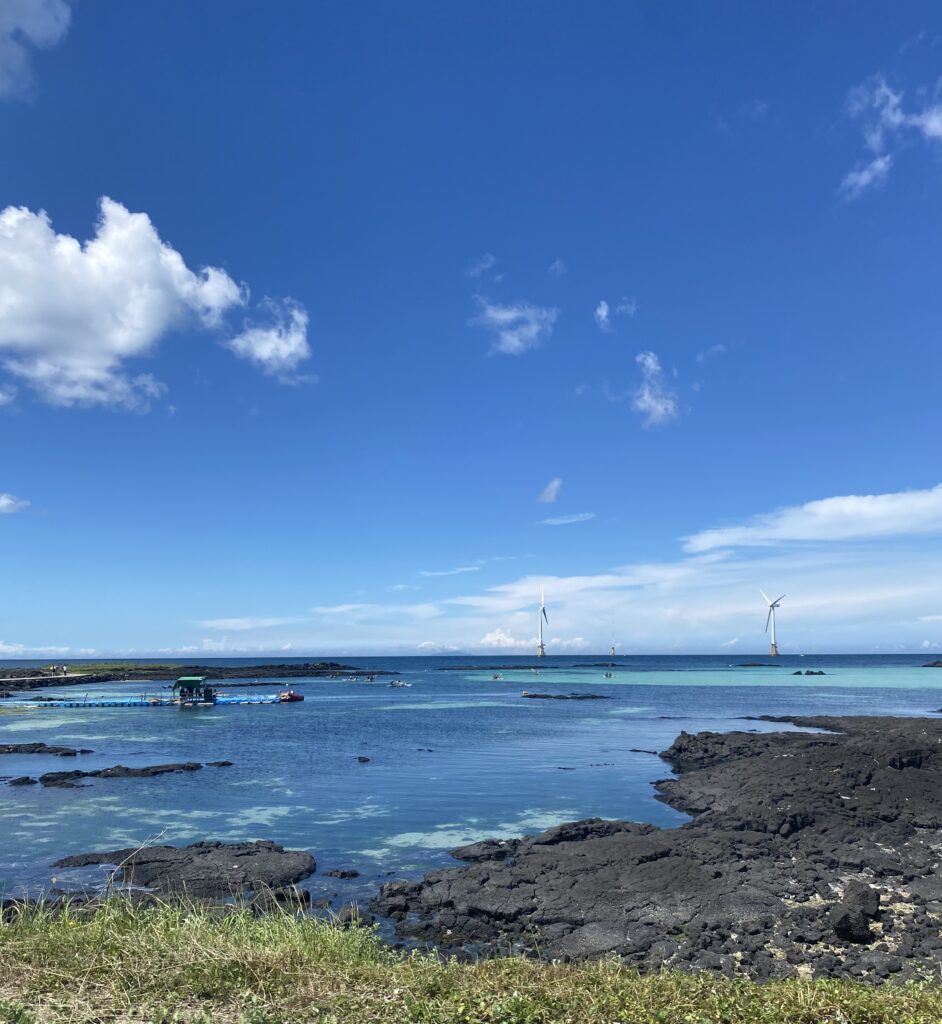 Woljeongri Beach where you can see clear water, wind turbines, and black basalt rock