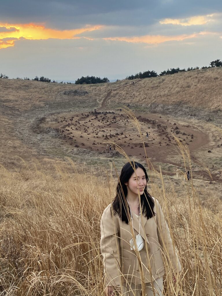 At the summit of Geum Oreum which is a natural landscape created by Mother Nature, a woman stands among reeds  