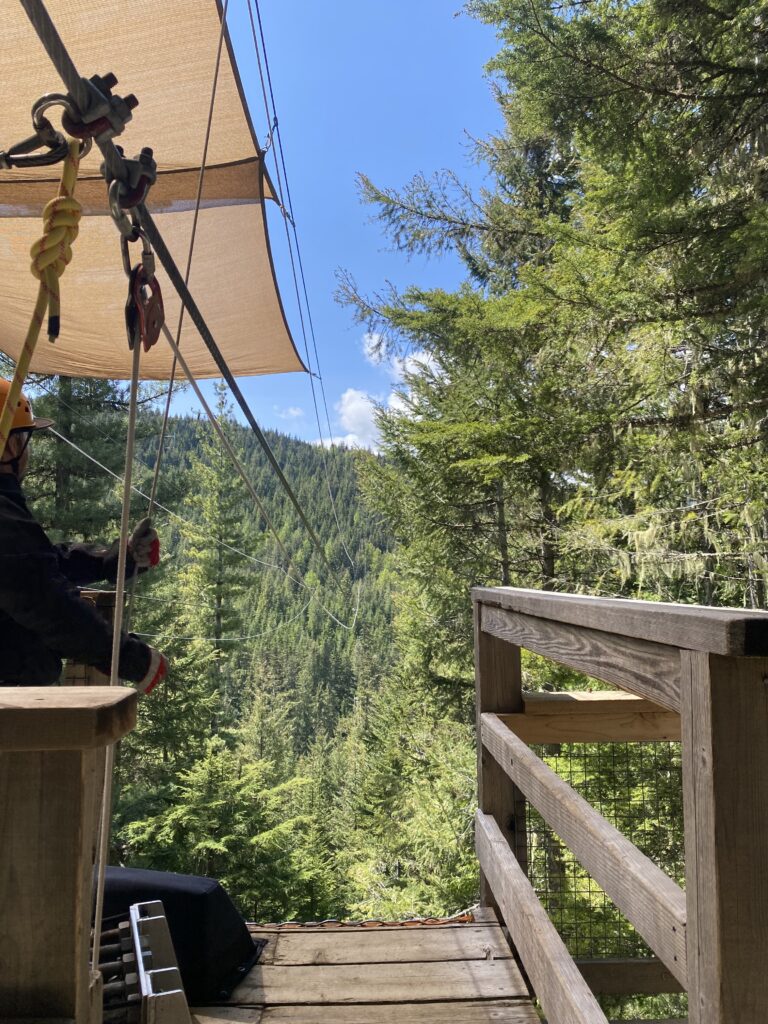 Zipline setup with ropes and pulleys on a wooden deck surrounded by a dense forest in Whistler, Canada.