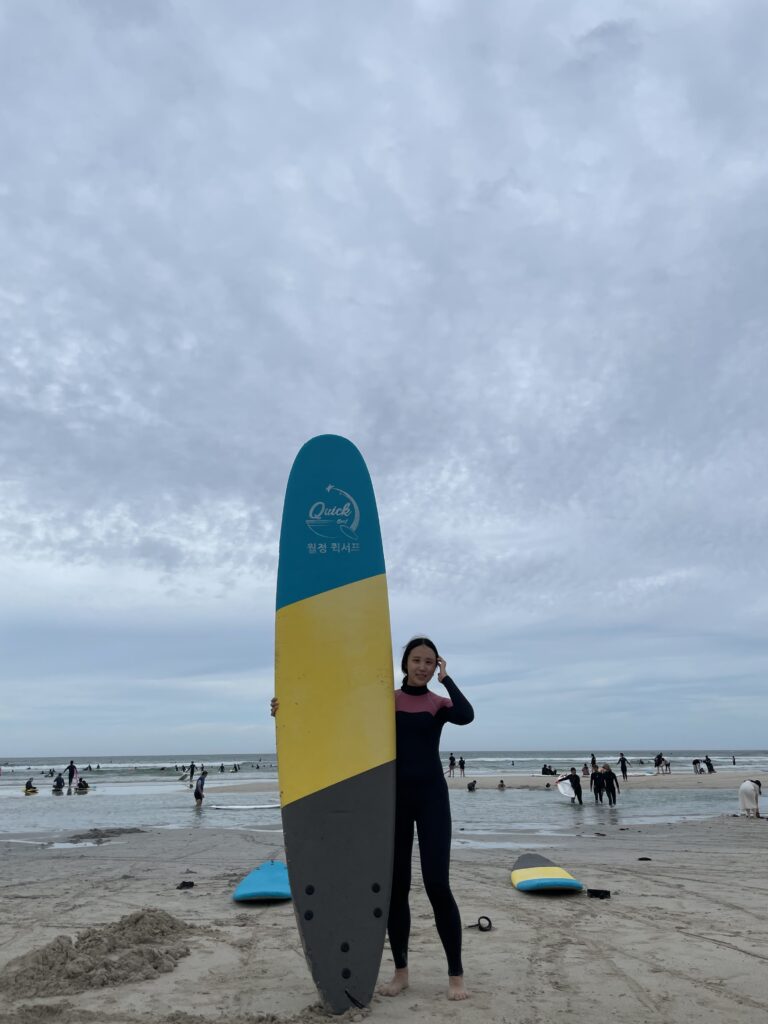 A woman standing on the beach in a wetsuit, holding a surfboard at Woljeongri Beach