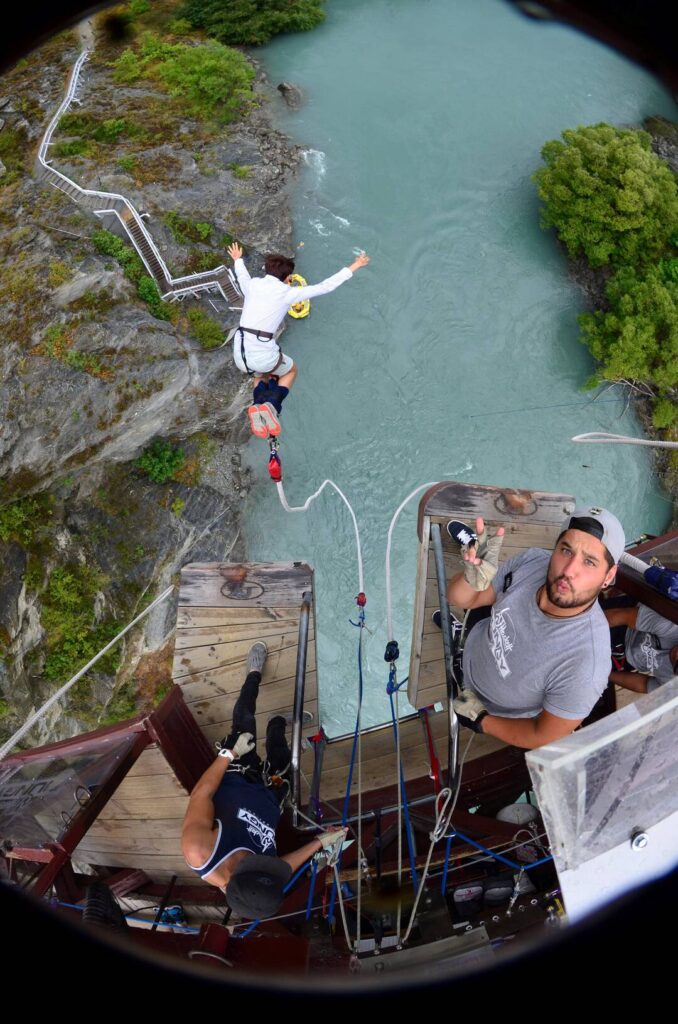 A person mid-air during a bungee jump, which is considered one of the most thrilling outdoor activities, with two instructors above