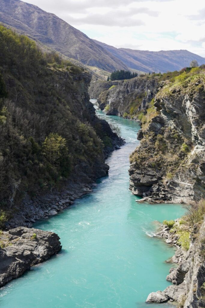 A canyon in Queenstown with steep rocky cliffs and a bright emerald river flowing through